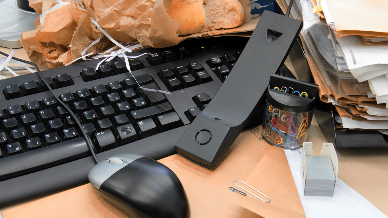 Messy desk showing computer, mouse, files, and bread